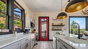 A modern kitchen with a red door, wooden cabinets, and a large window overlooking a residential area. - Stunning Mtn Lodge on Lake with two Story Dock, Indoor Pool, Arcade,and Hot Tub. (Sevierville)