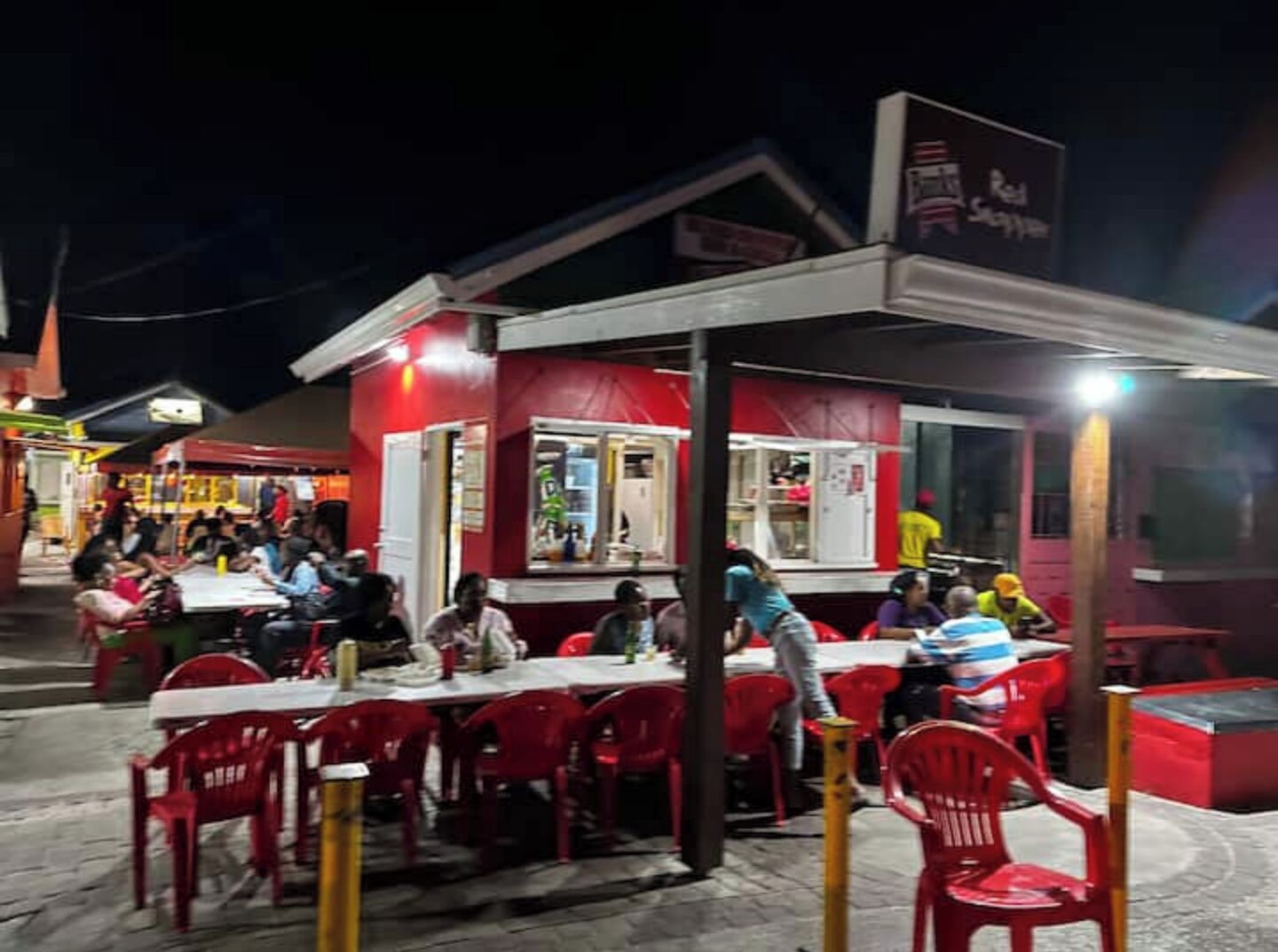 Un pequeño restaurante al aire libre con sillas y mesas rojas, una barra para ordenar comida y un letrero que indica Red Slipper.