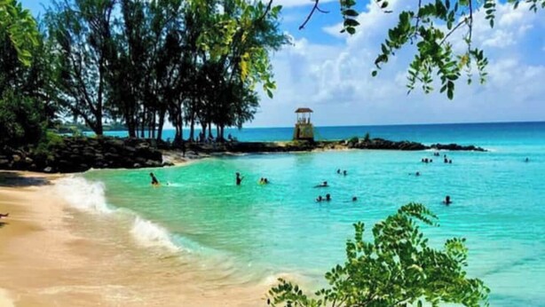 Una playa con agua turquesa cristalina, una orilla arenosa y un promontorio rocoso con vegetación.