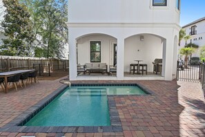 A pool area with a brick patio, a wooden deck, and a white building with arched doorways.