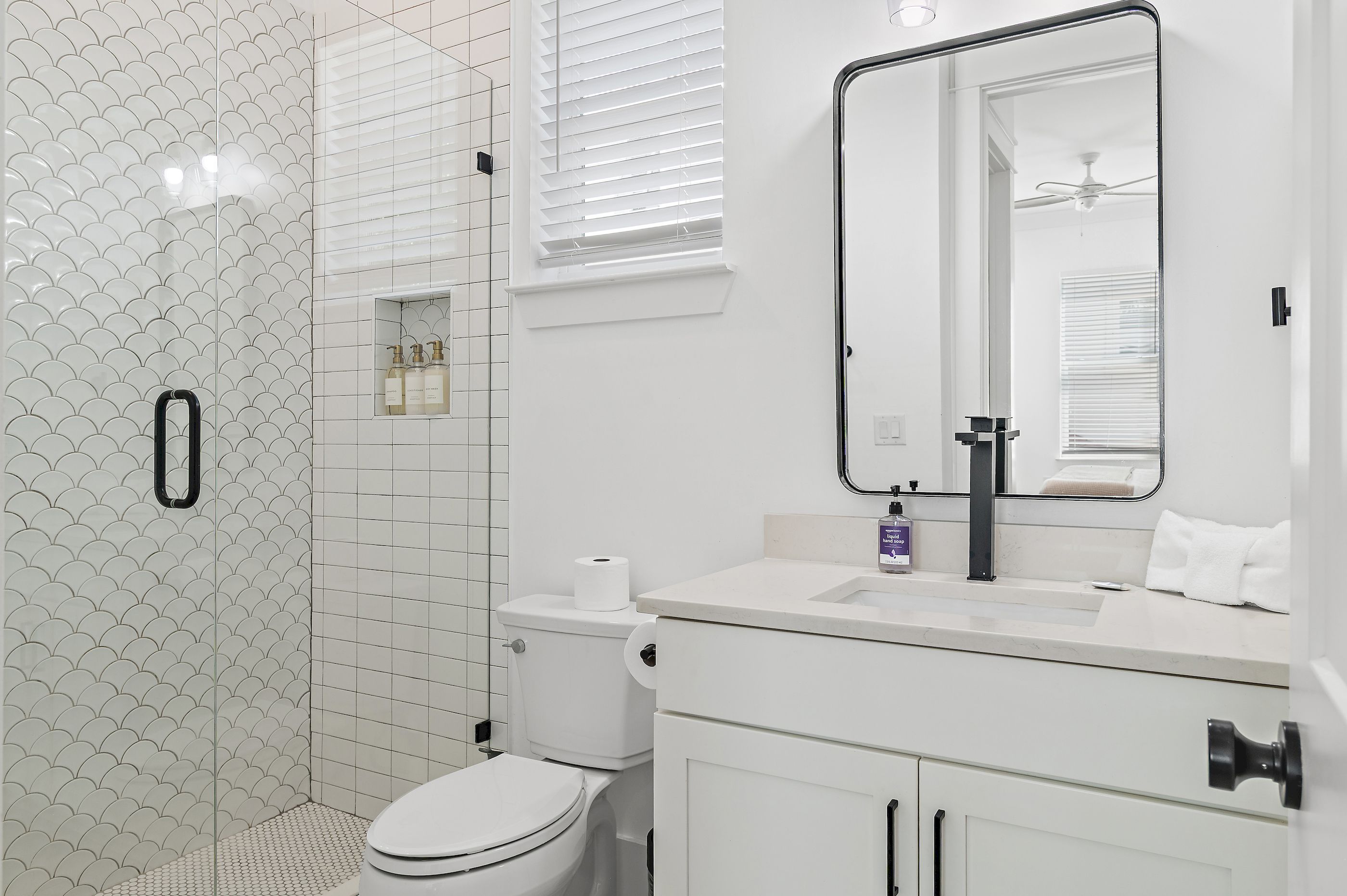 A modern bathroom with a toilet, sink, mirror, and shower area.