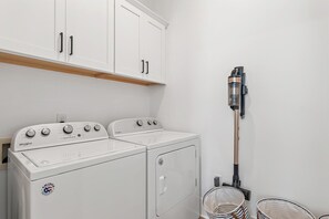 A laundry room with a white Whirlpool washer and dryer, a vacuum cleaner, and a wooden shelf above the cabinets. - Heated Private Pool*6-Seater Golf Cart*Steps2Beach (Santa Rosa Beach)