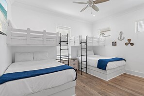 Une chambre avec des lits superposés, un ventilateur de plafond et une fenêtre avec des stores.