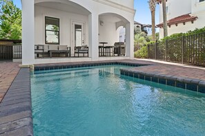 Une piscine avec un espace patio, un barbecue et une vue sur un immeuble d’habitation.