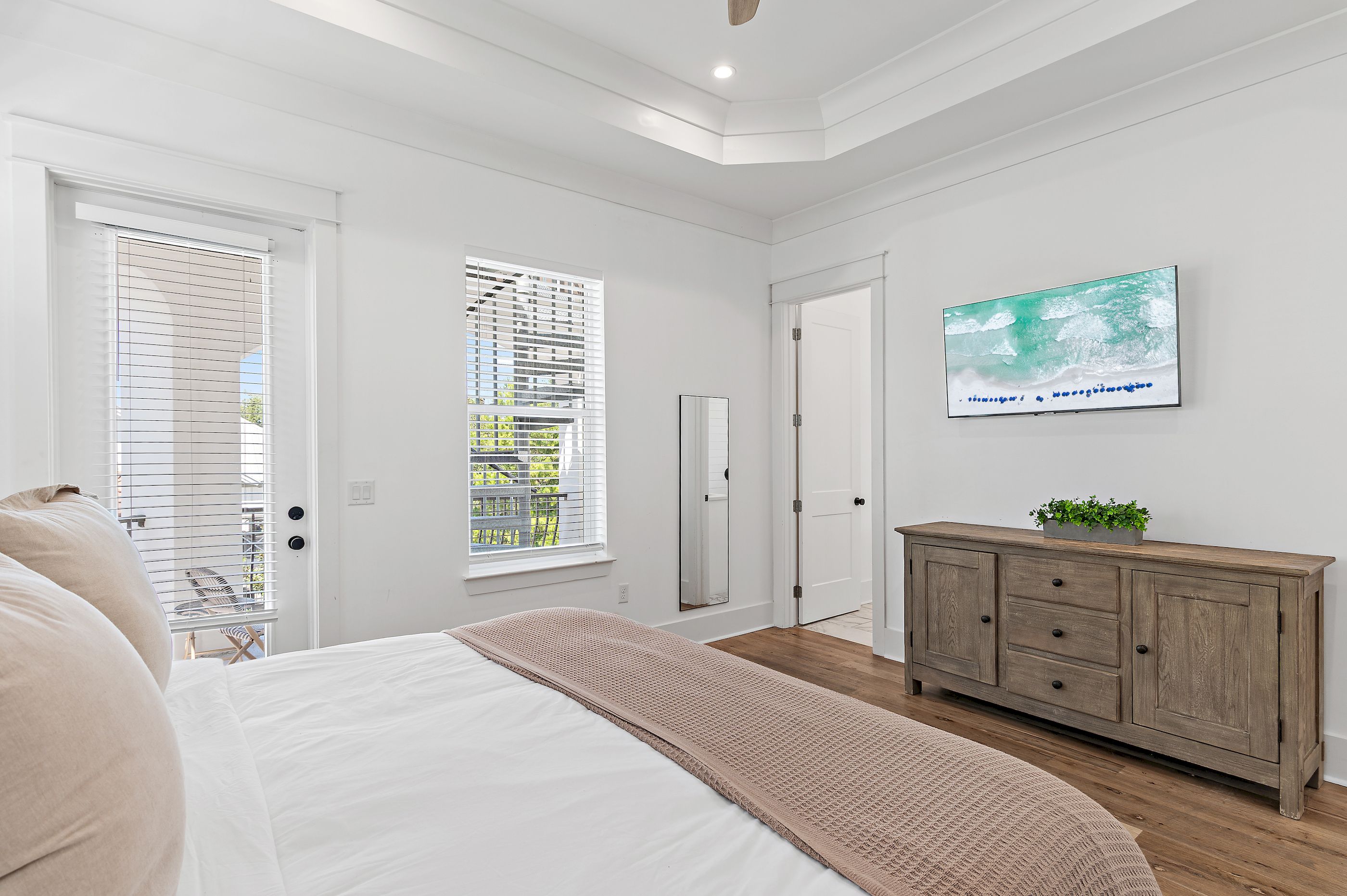 A bedroom with a bed, a dresser, a television, and two windows with blinds.