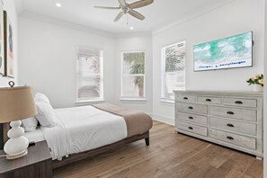 A bedroom with a bed, a dresser, a television, and three windows with blinds.