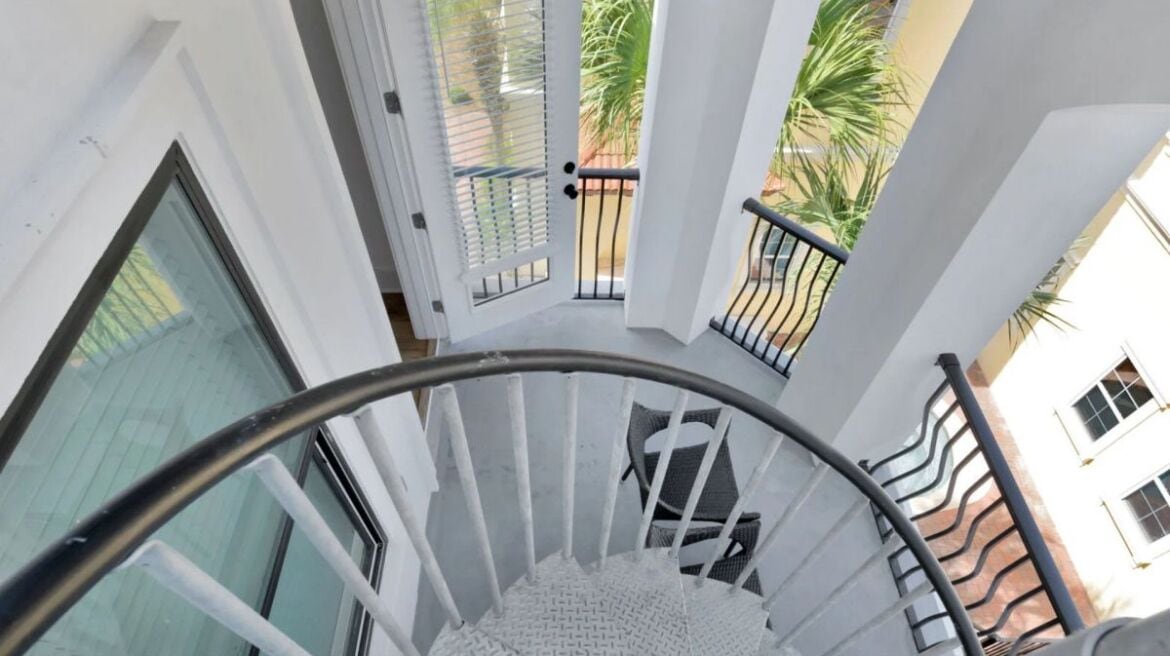 A spiral staircase with a metal handrail and white walls.