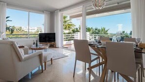 Una sala de estar moderna con televisor, asientos y un comedor con vista al mar.