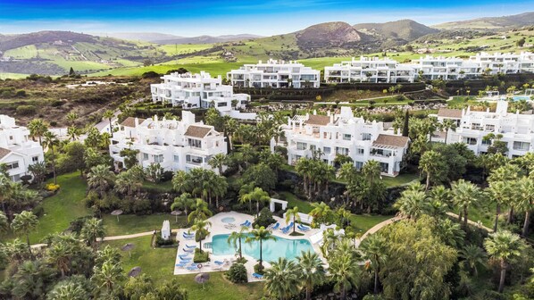 A resort with white buildings, a swimming pool, and lush greenery.