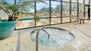 An indoor pool area with a hot tub, lounge chairs, and a large potted plant.