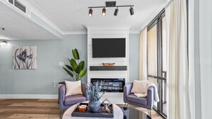 A modern living room with a fireplace, two armchairs, a coffee table, and a large window.
