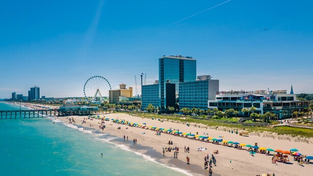 A beach with a pier, a Ferris wheel, and modern buildings in the background.