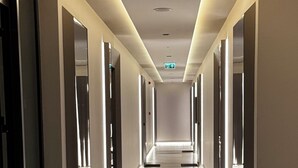 A long, well-lit hallway with a marble floor, emergency exit sign, and a fire alarm on the ceiling. - Elite Luxury Suites at Diamond in City (Accra)