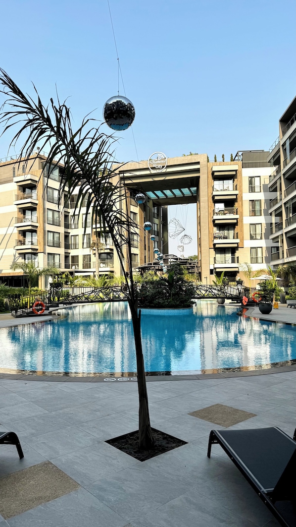 A modern hotel with a swimming pool, palm trees, and a disco ball.