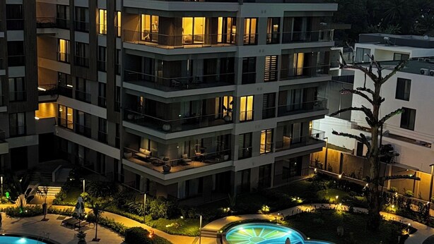 A multi-story hotel with a swimming pool area, including a large pool and smaller pools, surrounded by well-lit pathways and outdoor seating areas. - Elite Luxury Suites at Diamond in City (Accra)