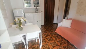 Een compacte woonruimte met een kitchenette, een eettafel met stoelen, een bank en een vloer met een patroon.