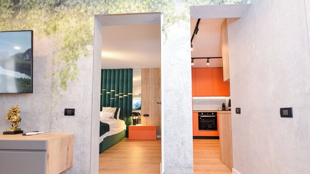 A modern interior with a wooden floor, a green bed, a small orange table, and a kitchen area with orange cabinets. - StarDust Apartment - Cismigiu Gardens (Unknown)