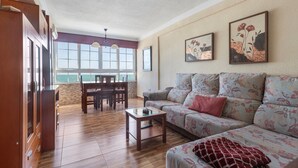A living room with a sofa, a coffee table, a dining area with chairs, and a kitchen area with cabinets. - Beachfront apartment with incredible views of Málaga Bay (Málaga)