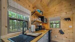 Cocina compacta con lavamanos, estufa y armarios de madera, con ventanal y una decoración de oso en la pared.