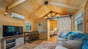 Acogedor interior de cabaña con televisor, paredes de madera, comedor y dormitorio.