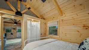 Un dormitorio tipo cabaña de madera con una cama, una ventana y una puerta que da a otra habitación.