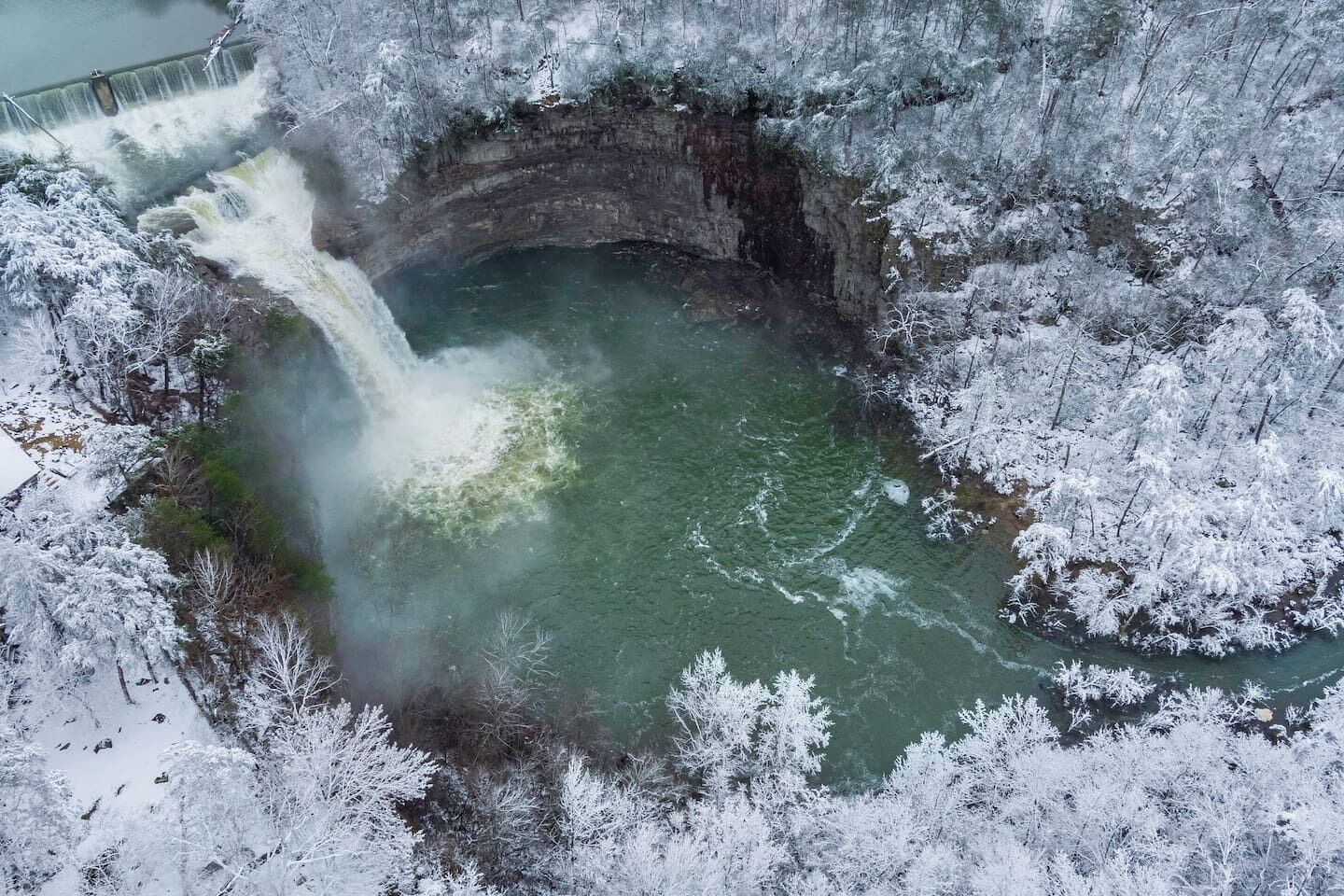 Una cascada que se precipita en una piscina circular rodeada de árboles cubiertos de nieve.