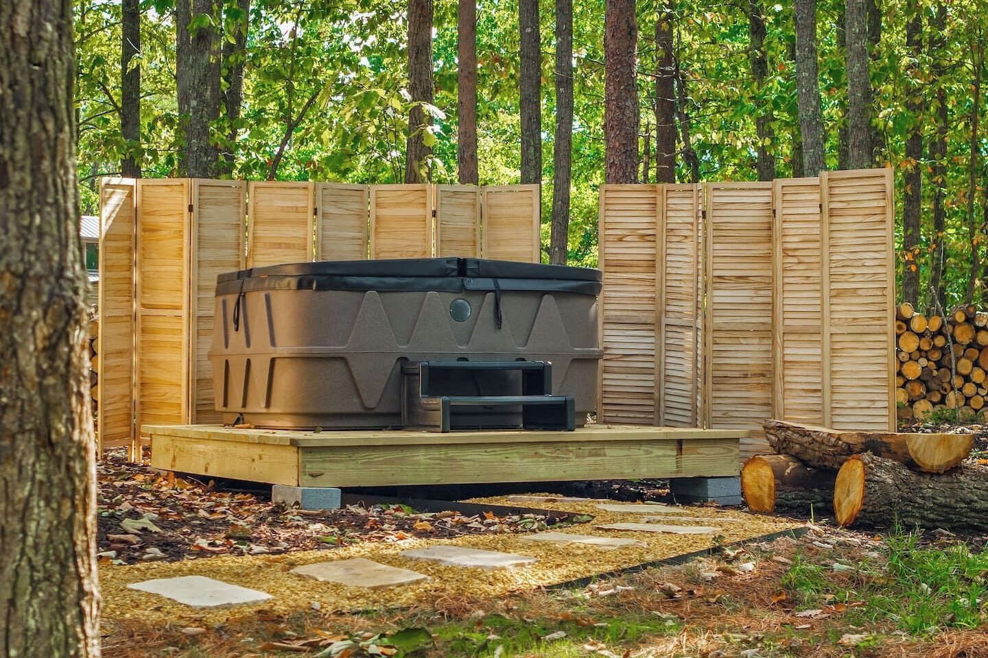 Een hottub op een houten platform, omringd door een houten omheining in een bebost gebied.