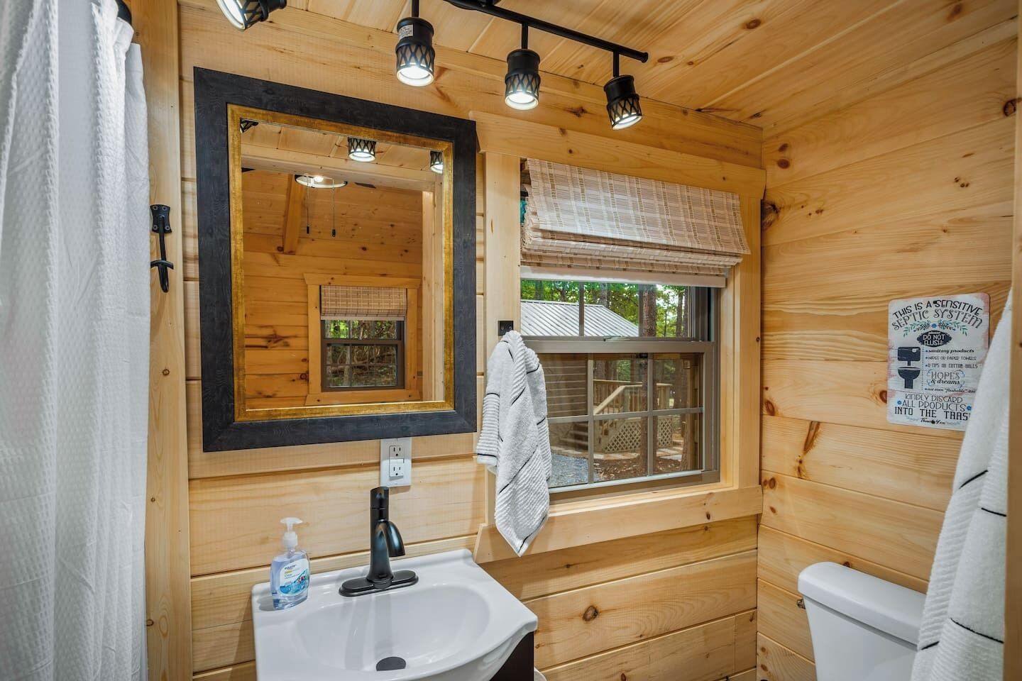 Une salle de bain rustique, avec une cabine en bois, un lavabo, un miroir et une fenêtre.