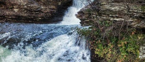 Een waterval stort neer over rotsachtig terrein met weelderige begroeiing.