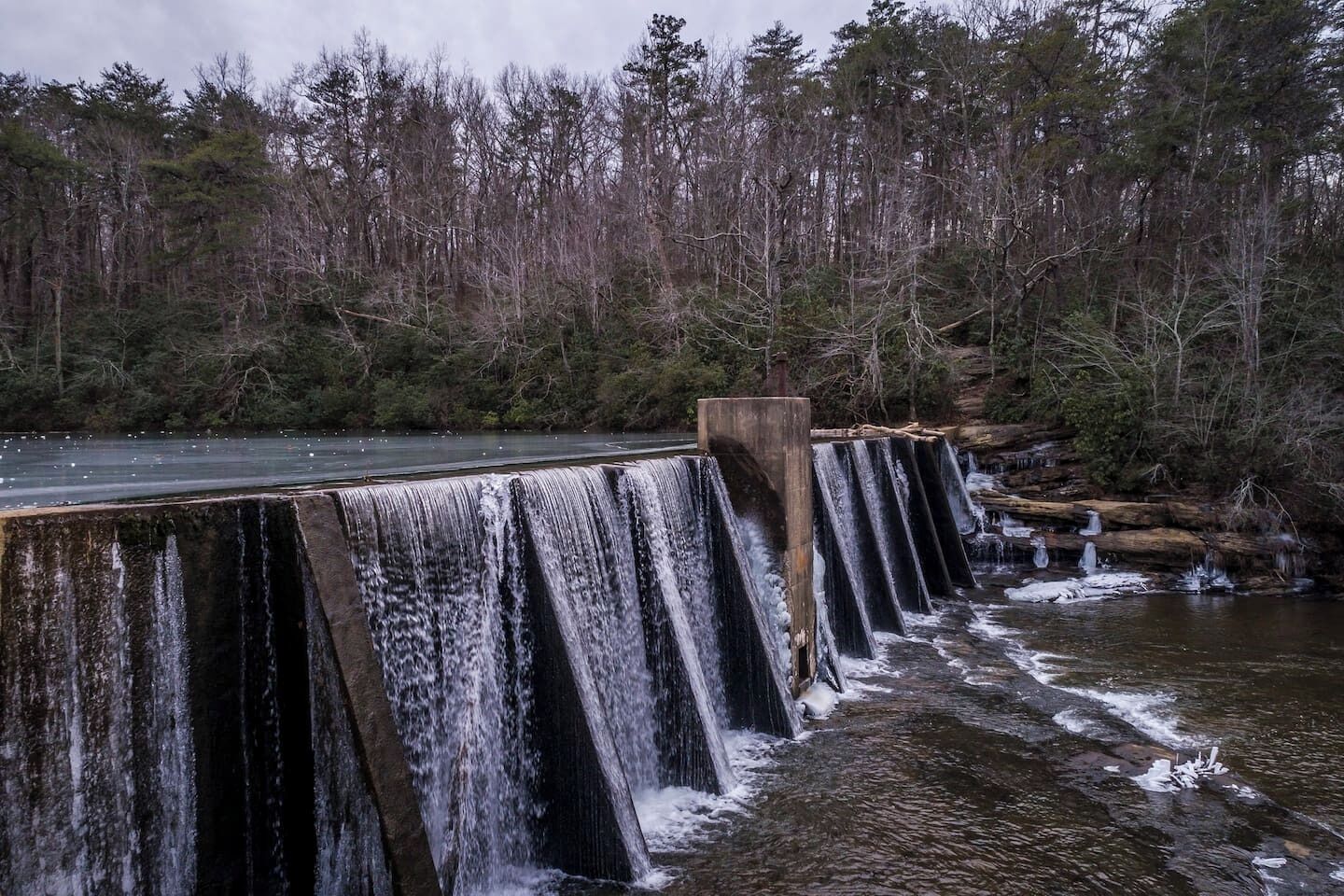 A dam with multiple water channels and a forested area in the background.