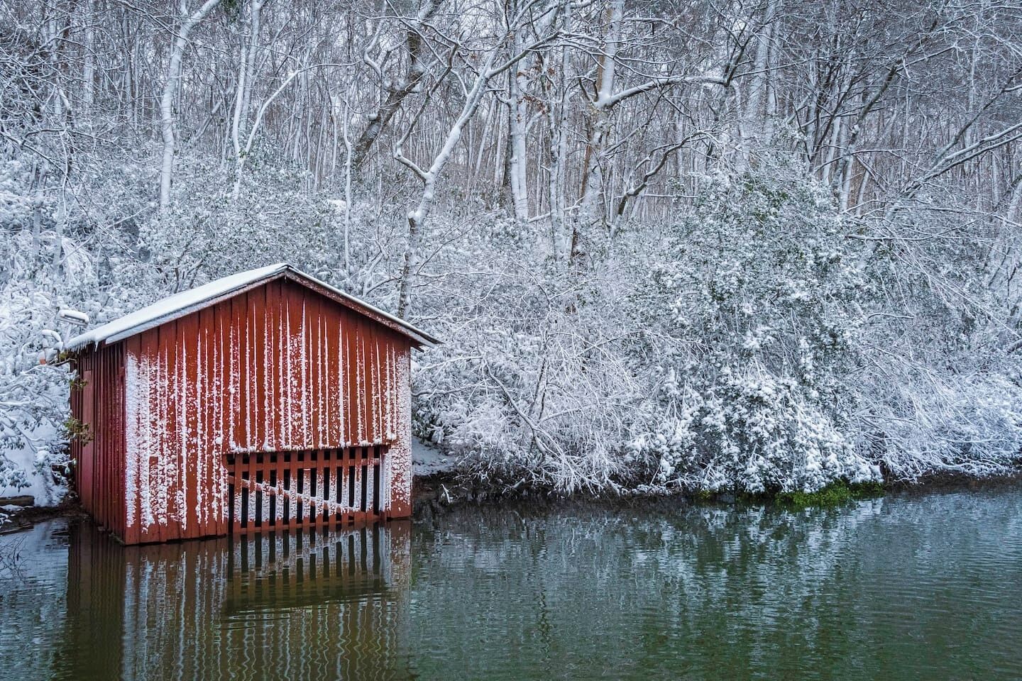 Un cobertizo rojo de madera junto a la orilla nevada de un río.