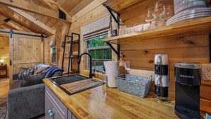 A cozy cabin interior with a wooden interior, a kitchenette with a sink, a coffee maker, and a shelf with dishes and glasses.