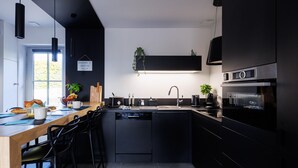 A modern kitchen with black cabinetry, a wooden dining table, and a black island with a sink.