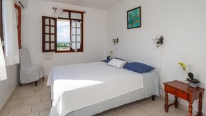 A bedroom with a bed, a chair, a nightstand, a window with curtains, and a painting on the wall.