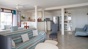 A spacious living area with a sofa, chairs, a small table, and a kitchen in the background.