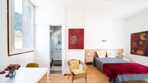 Un dormitorio con cama, una silla, una mesa con un florero y obras de arte en las paredes.