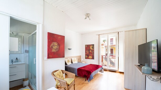 Un dormitorio con cama, una silla, televisor y ventana.