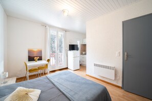 Huone, jossa on sänky, työpöytä, tuoli, televisio, jääkaappi ja ovi.