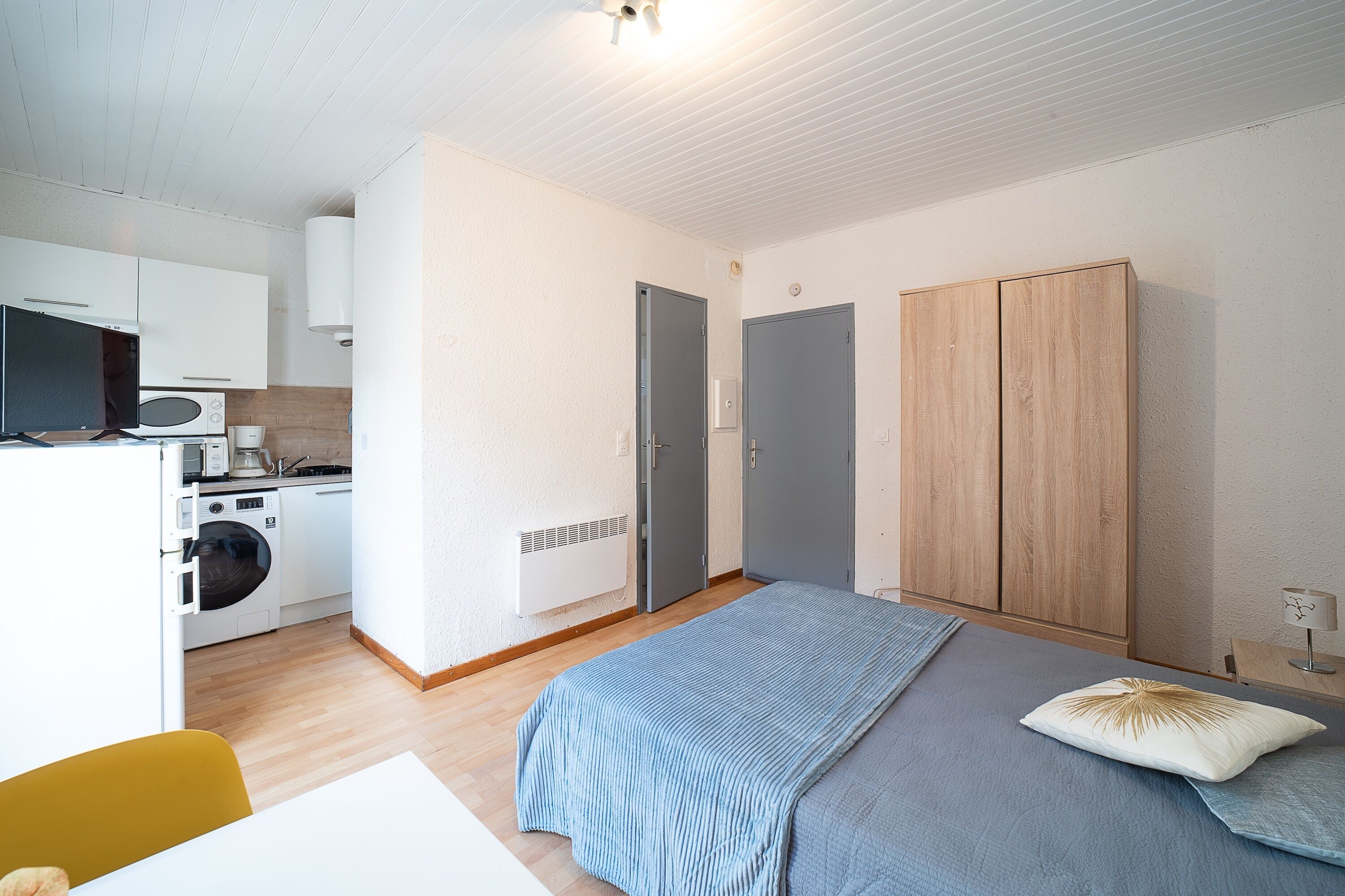 A compact room with a bed, a washing machine, and a kitchenette.