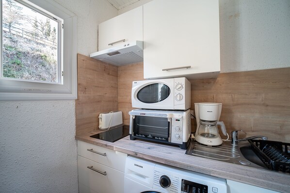 A compact kitchen with a microwave, toaster, and coffee maker on the countertop, a dishwasher below, and a window with a view of trees.