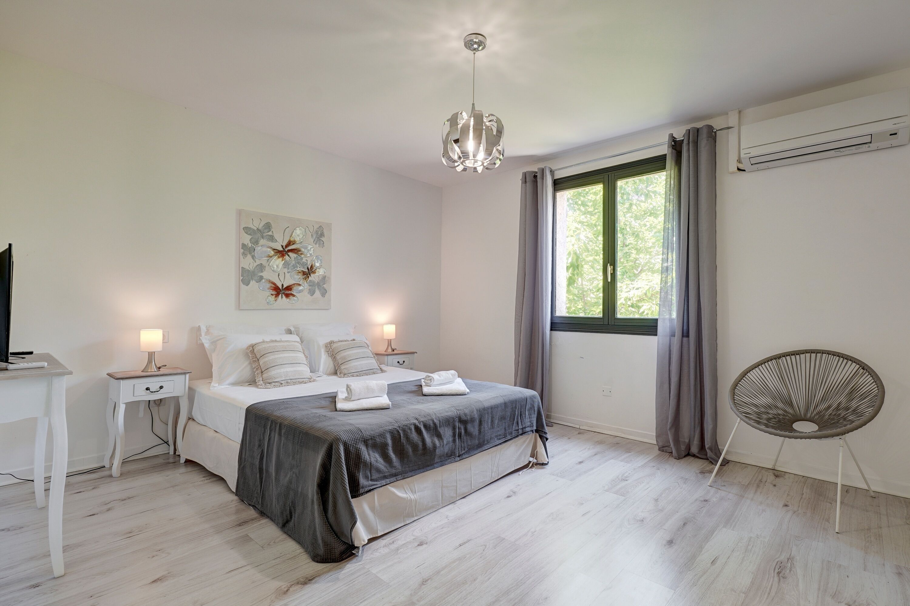 Un dormitorio con cama, mesitas de noche, lámpara colgante, ventana con cortinas y equipo de aire acondicionado.