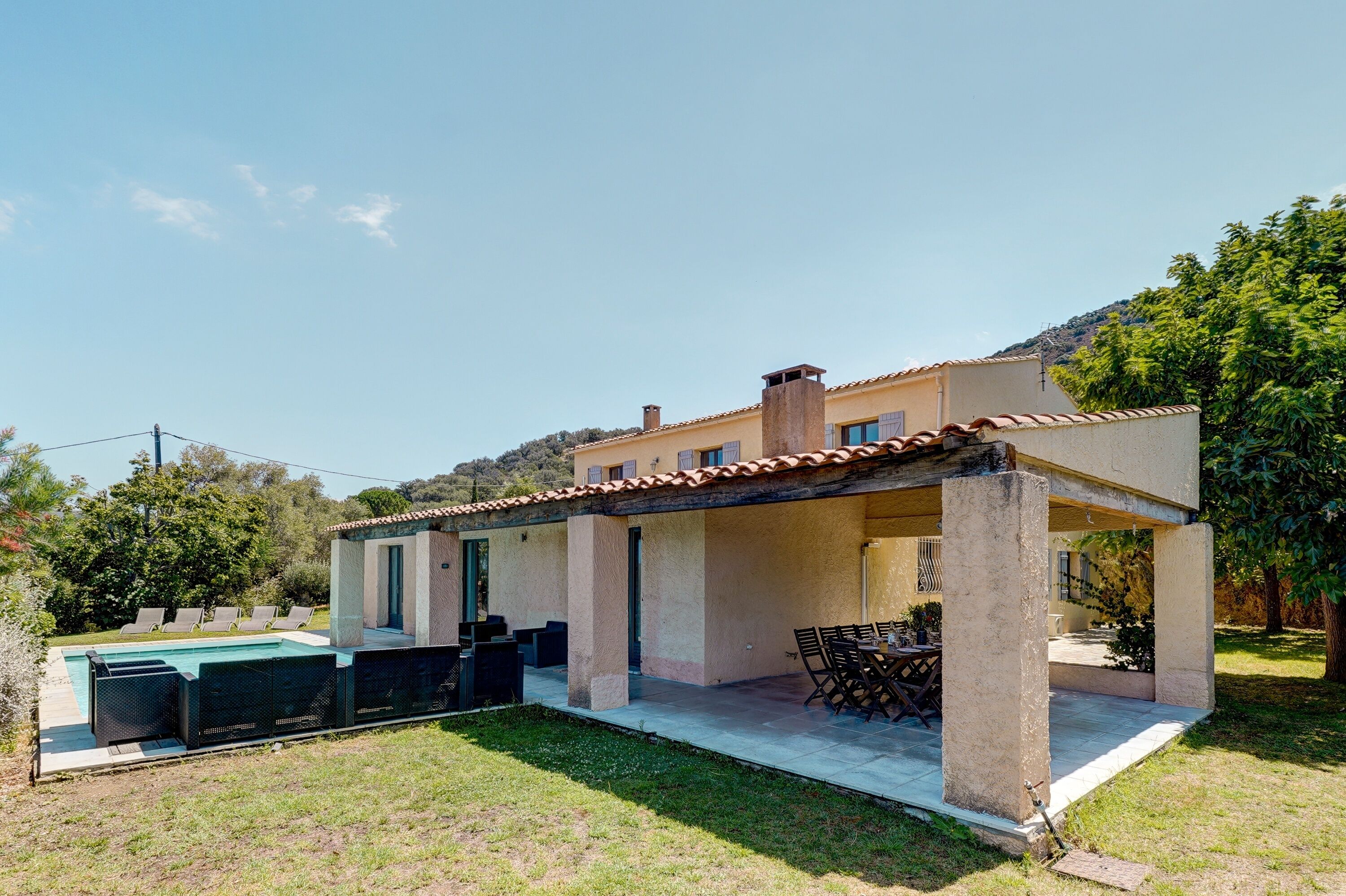 Ein modernes Haus mit überdachter Terrasse, Swimmingpool und Garten.
