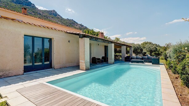 A poolside area with a wooden deck, outdoor seating, and a mountain backdrop.