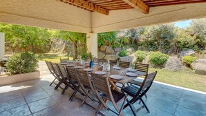 An outdoor patio with a covered dining area, stone walls, and a garden view.