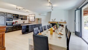 A modern kitchen with dark cabinets, a central island, and a dining area with a long table and chairs.