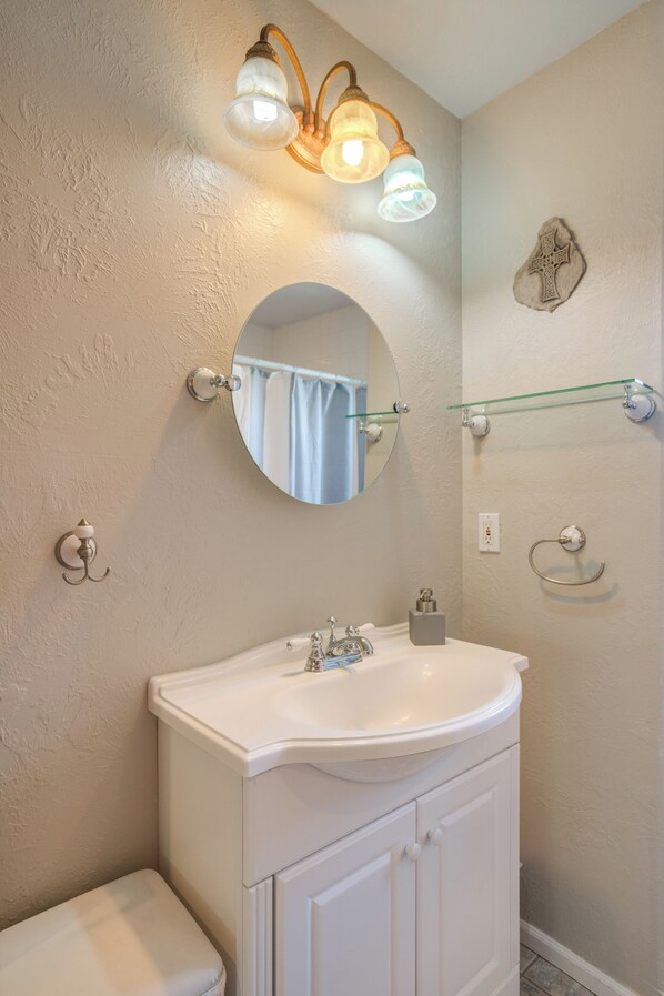 A bathroom with a white sink, a round mirror, and a light fixture above the mirror. - Charming 2-bedroom house with WiFi, AC in wonderful Pateros (Pateros)