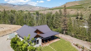 Une maison dotée d’un grand porche et d’un espace extérieur couvert, entourée d’un paysage montagneux et d’une forêt dense.