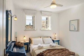 Een slaapkamer met een bed, twee nachtkastjes, een spiegel en twee ramen met gordijnen.