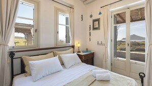 A bedroom with a bed, bedside table, lamp, and a view of the outdoors. - Isterni | 3BR House with Sea View & BBQ | Blue Coral 2 (Paros)