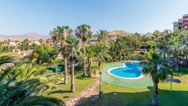 Een resort met een zwembad, palmbomen en een bergachtig landschap op de achtergrond.